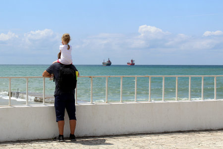 Dad and daughter stand on the embankment and look at the sea.