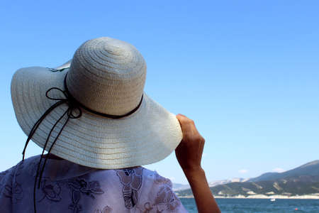 The girl on the beach stands holding a Panama hat and looks into the distance.の写真素材