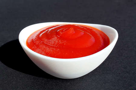 Tomato sauce is poured into a white plate on a black background.の写真素材