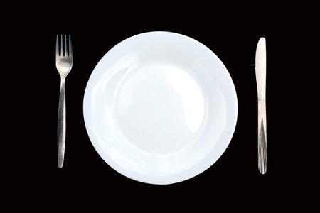 White plate with a fork and a knife lie on a black background.