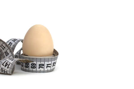 A chicken egg wrapped in a centimeter tape stands on a white background.の写真素材