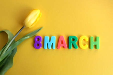 On a yellow background lies a yellow tulip and the inscription 8 March.の写真素材