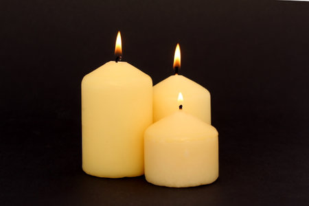 Three wax candles are burning on a black background.の写真素材