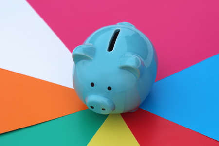 A blue piggy bank is standing against a bright multi-colored background.の写真素材