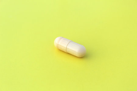 The drug in a beige capsule lies alone on an isolated yellow background.の写真素材