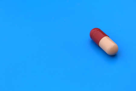 The drug in a two-color capsule lies alone on an isolated blue background.の写真素材