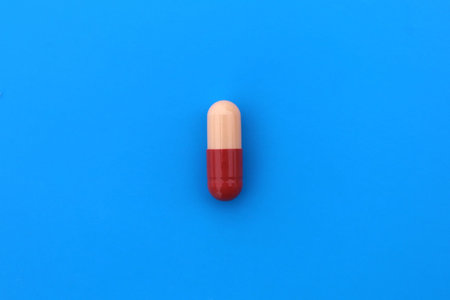 The drug in a two-color capsule lies alone on an isolated blue background.の写真素材