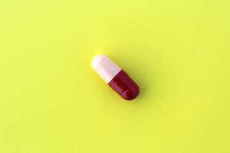 The drug in a capsule beige with burgundy color lies alone on an isolated yellow background.の写真素材