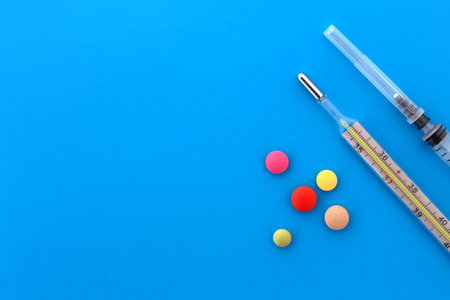 On a blue background are pills, a thermometer and a syringe.の写真素材