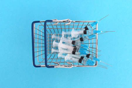 A miniature shopping basket stands on a blue background with a bunch of syringes. view from above.の写真素材