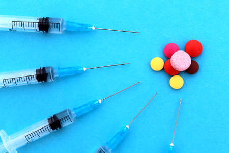 Several syringes lie on a blue background and different pills lie nearby.の写真素材
