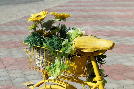 A yellow decorative bicycle with flowers stands in a parking lot on a summer day.の写真素材