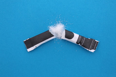 Scattered sugar in a disposable torn bag lies on a blue background.の写真素材
