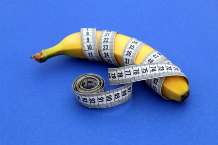 A yellow ripe banana with a centimeter flexible tape lies on a blue background.の写真素材