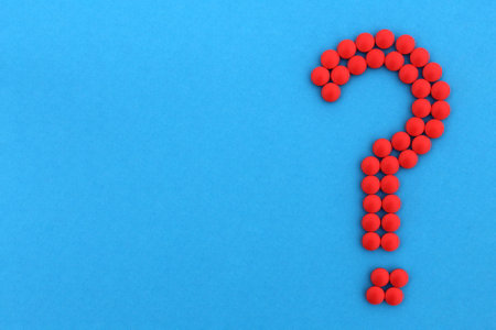 Of the red medicine pills lined with a question mark on a blue background.の写真素材