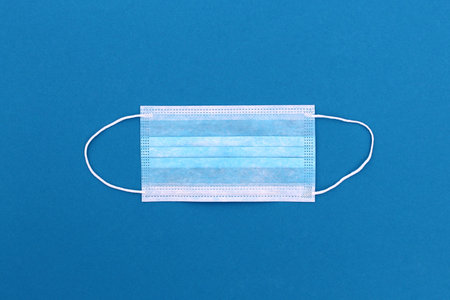 Medical mask lies on a blue background, top view.