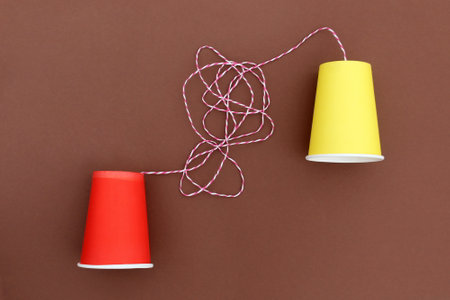 An impromptu telephone made of bright paper glasses with a rope on a brown background.の写真素材