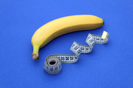 A yellow ripe banana with a centimeter flexible tape lies on a blue background.の写真素材