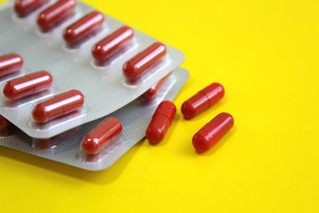 Red medicine capsules lie on a yellow background.の写真素材
