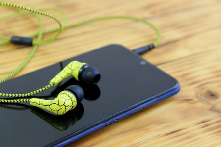 A cell phone with headphones lies on a wooden tableの写真素材