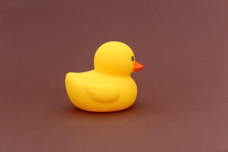 A yellow rubber duck stands on a brown background.の写真素材