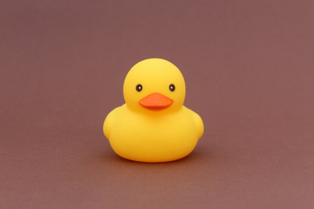 A yellow rubber duck stands on a brown background.の写真素材