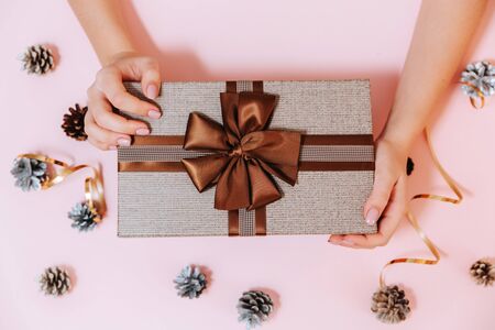 Box with a bow in the hands of a young girl on a pink background. New year gift.の写真素材