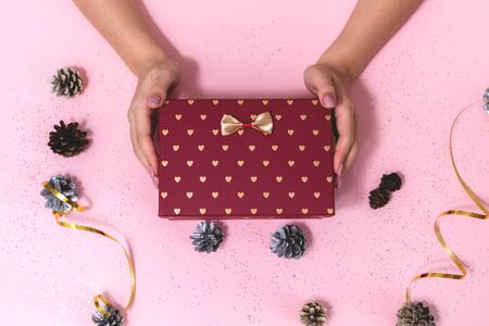Box with a bow in the hands of a young girl on a pink background. New year gift.の写真素材
