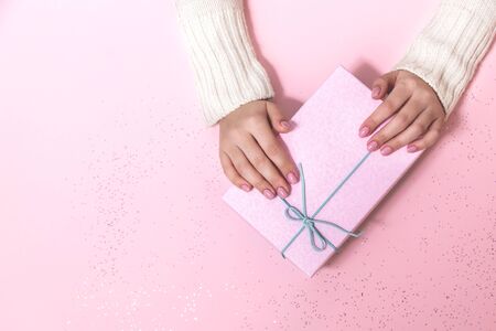 Box with a bow in the hands of a young girl on a pink background. New year gift.の写真素材
