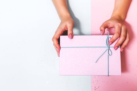 Box with a bow in the hands of a young girl on a pink background. New year gift.の写真素材