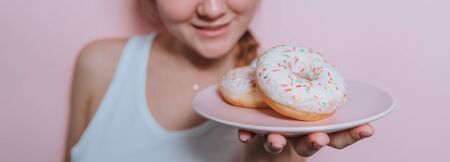Chocolate doughnut on a brown saucer on a pink table. The girl with the pink Cup wants to eat a doughnut.の写真素材