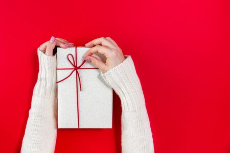 Gift box in the hands of a young girl on a red background.の写真素材