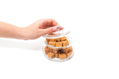 Sugar cubes in a glass jar. Jar of sugar in the hands of a girl on a white background.の写真素材