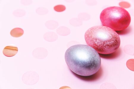 Three pink Easter eggs on the pink table with confetti.の写真素材