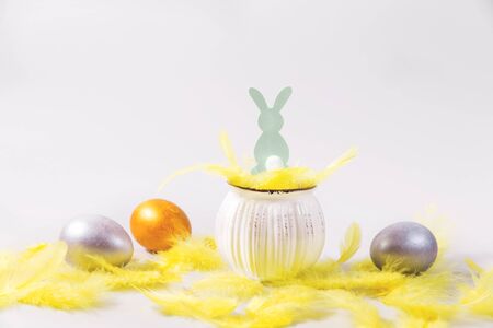 Three Easter eggs in pastel colors, yellow feathers, an Easter rabbit in a nest on a gray background.の写真素材