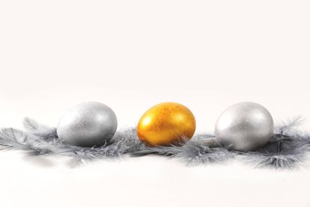 Three silver and gold Easter eggs on a gray background in silver feathers.の写真素材