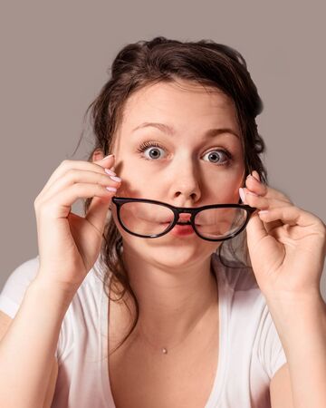 The girl takes off her glasses with her hands on a gray background Home environment.の写真素材