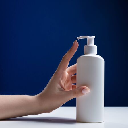 Plastic white antiseptic bottle with a dispenser on a blue background. The white package is on a white table.の写真素材