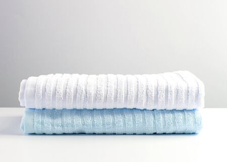 White and light blue towels are on the white table. Front view.の写真素材