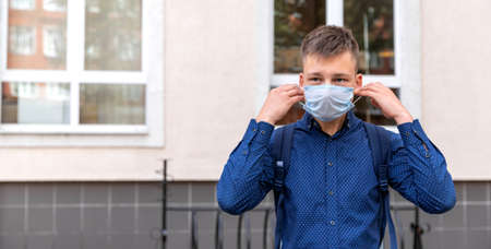 One teenager is near his school. He puts a medical mask on his face. This is a necessary rule of the new reality 2020. Medical concept.の写真素材