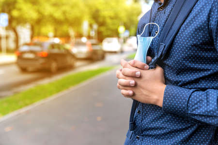 One teenager stands on a city street with a medical mask in his hands. He is ready to go to school and meet friends. Medical concept 2020.の写真素材