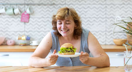 Happy curvy woman holding a Burger. Her eyes are closed and she's smiling. The girl likes junk food. She does not use a healthy diet.の写真素材
