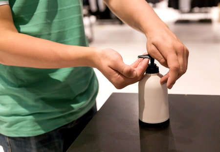 A teenager treats his hands with a sanitizer when entering a clothing store.の写真素材