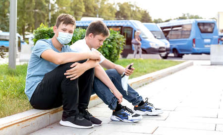 Two teenagers on the street of the city make a taxi order by phone. Their faces are covered in medical masks. The concept 2020.の写真素材