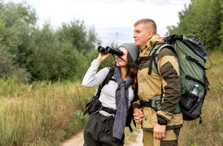 A young man and his girlfriend are sitting looking at the river through binoculars. They walked for...