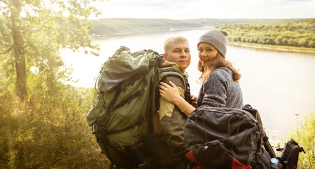 A young girl and her boyfriend are walking in the park, enjoying nature. They have large tourist backpacks. They're going camping.の写真素材