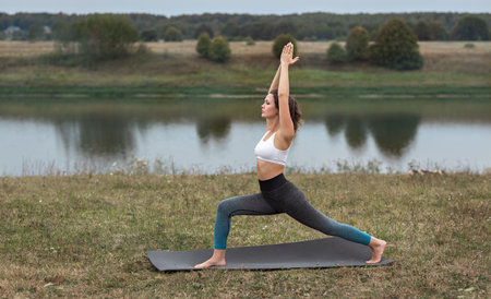 Young sporty woman doing fitness exercises near the river against the background of the forest....