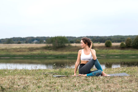 Young sporty woman doing fitness exercises near the river against the background of the forest....