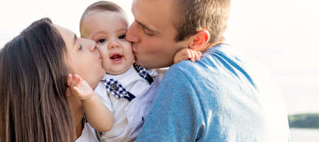 Mom and dad kiss their baby. They walk together outside the city. Close up.の写真素材