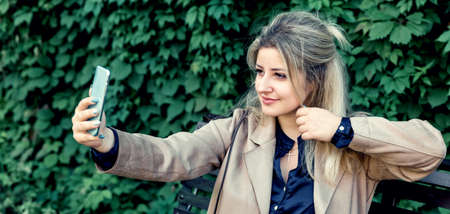 A beautiful girl takes a selfie in the Park against the background of green plants.の写真素材